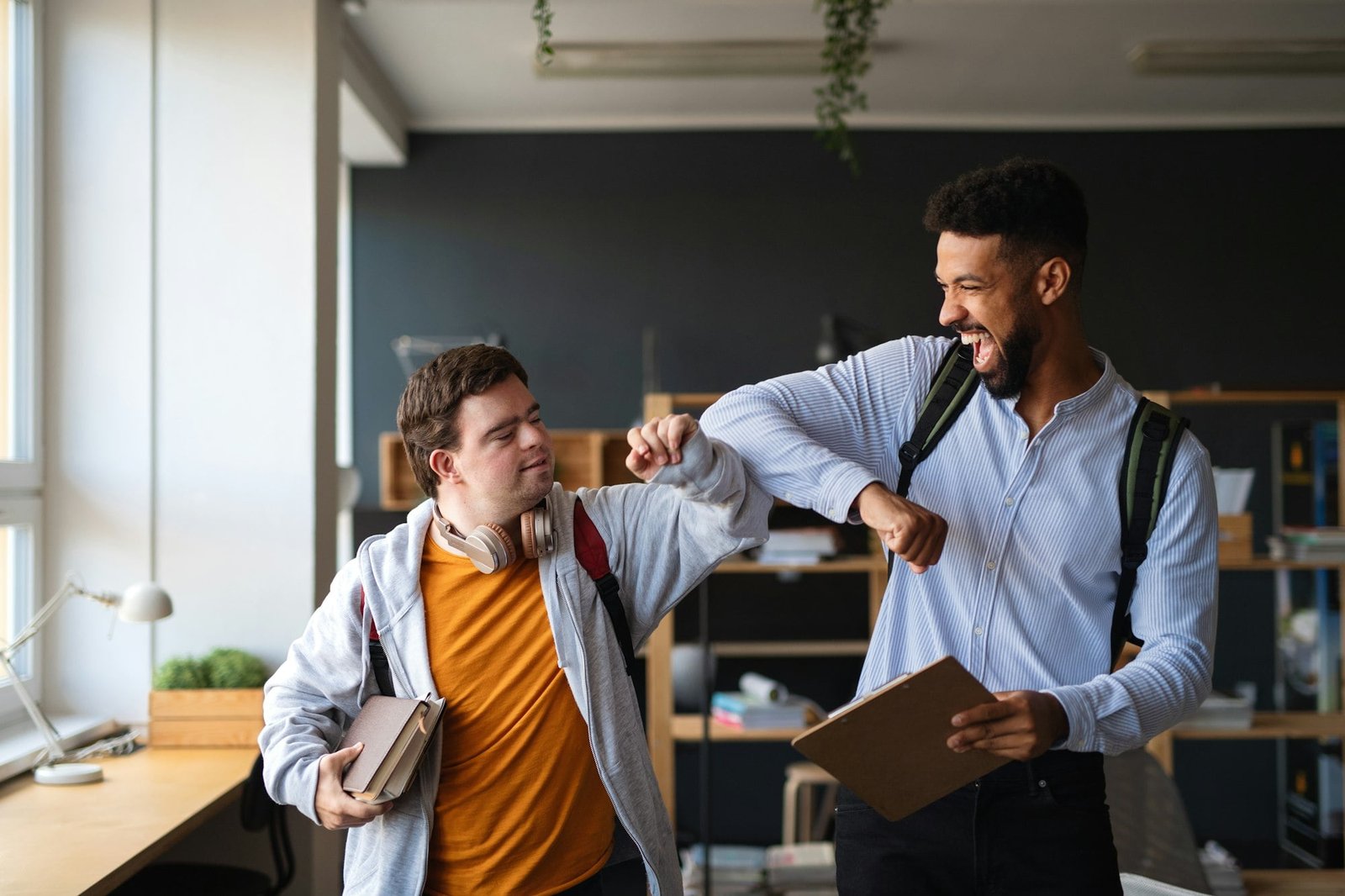 Young happy man with Down syndrome with his mentoring friend celebrating success indoors at school