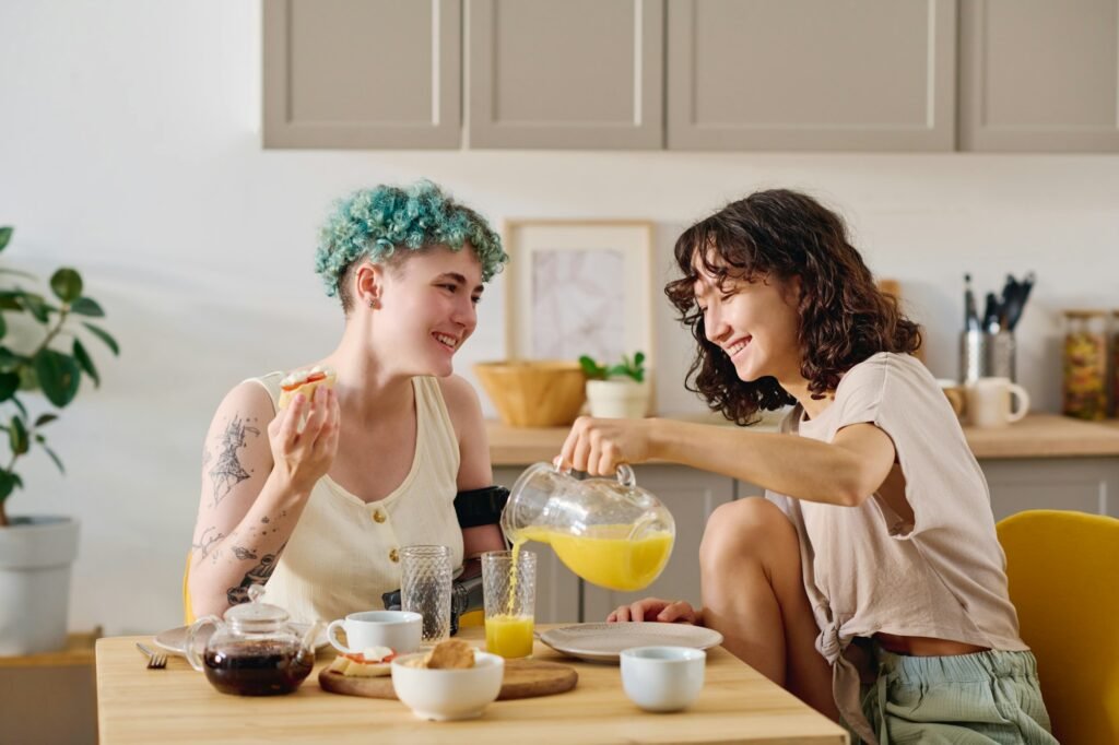 Young smiling woman pouring juice into glass of her girlfriend with disability